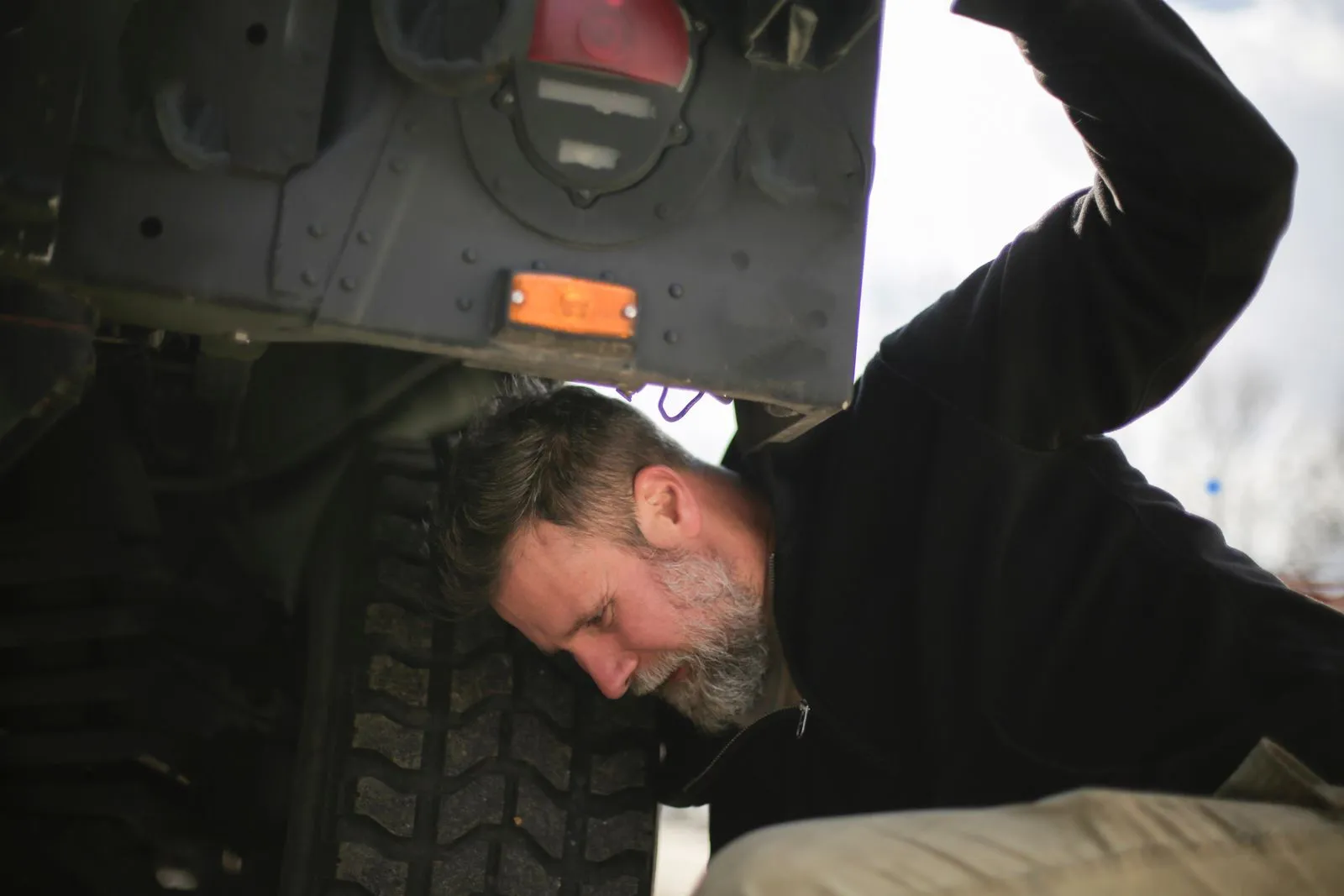 Side view of serious adult bearded mechanic in workwear repairing wheel of car while working on street near garage